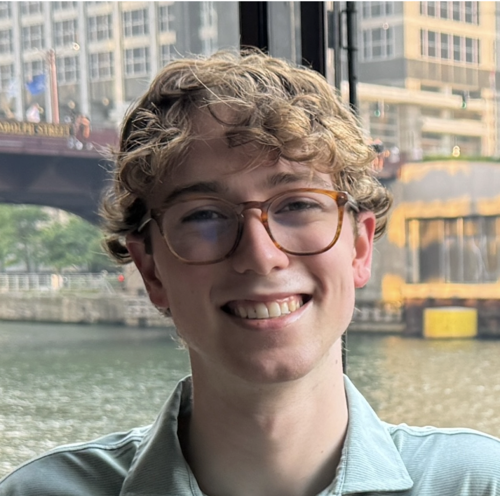 Paul Wallace smiles for a headshot in front of a river and bridge.